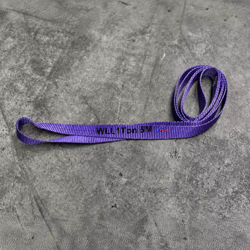 one tonne round webbing sling in the violet of its band, a flat webbing sling with an eye at each end and the working load limit printed along the webbing, lying on a concrete floor