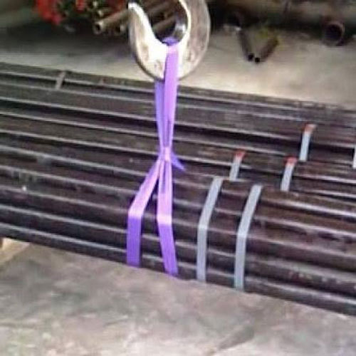 one tonne round webbing sling in use, wrapped round a bundle of steel tube and hanging from a crane hook in a yard, the violet band under load