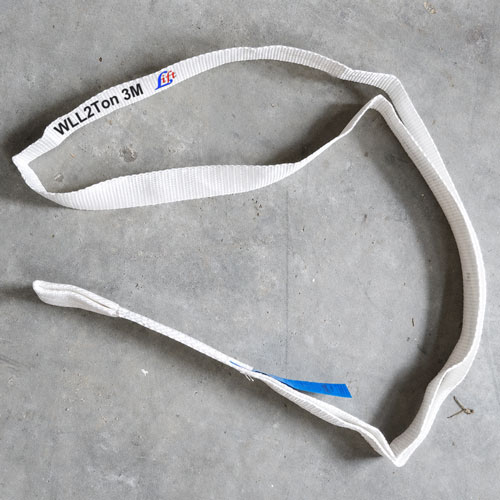 A white flat woven lifting sling printed with a working load limit and a length in black along its face, the band cl
osed into a loop and laid on grey concrete