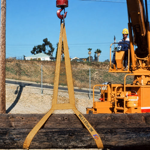 A flat woven loop in service as a two leg arrangement, the legs running from a hook down under a large timber log at
two positions, with an orange hydraulic loader and its operator behind