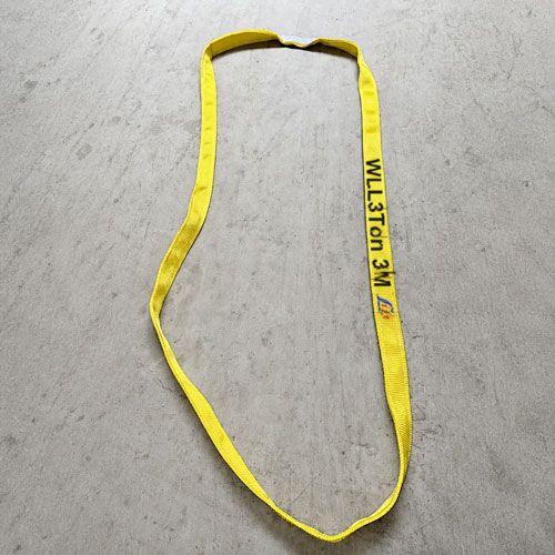 A closed flat woven webbing loop in yellow with WLL 3Ton 3M printed in black along the face and the maker's mark besi
de it, laid out on a grey concrete floor