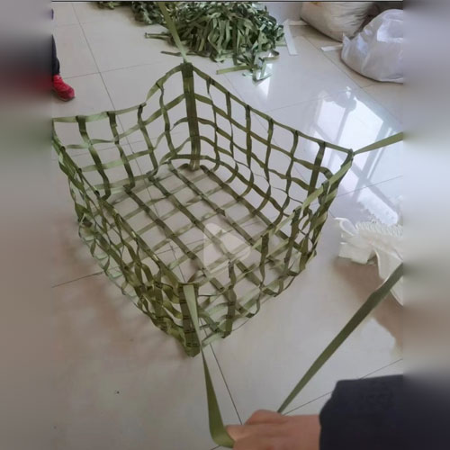 The same dark green flat webbing formed into a three dimensional open bag with a square base and four walls, held by
hand in a workshop, showing that the construction is built in more than one configuration